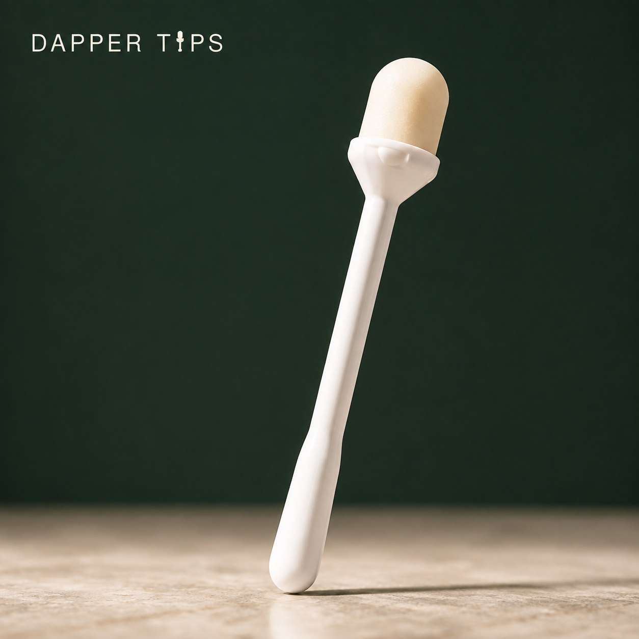Close-up of the white Dapper Tips single-use applicator with its balm tip, against a deep green backdrop
